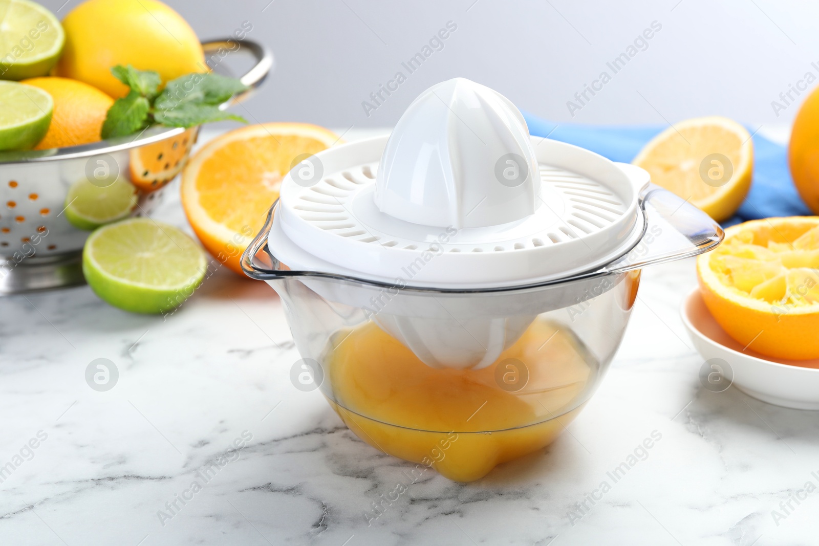 Photo of Plastic juicer and different citrus fruits on white marble table, closeup