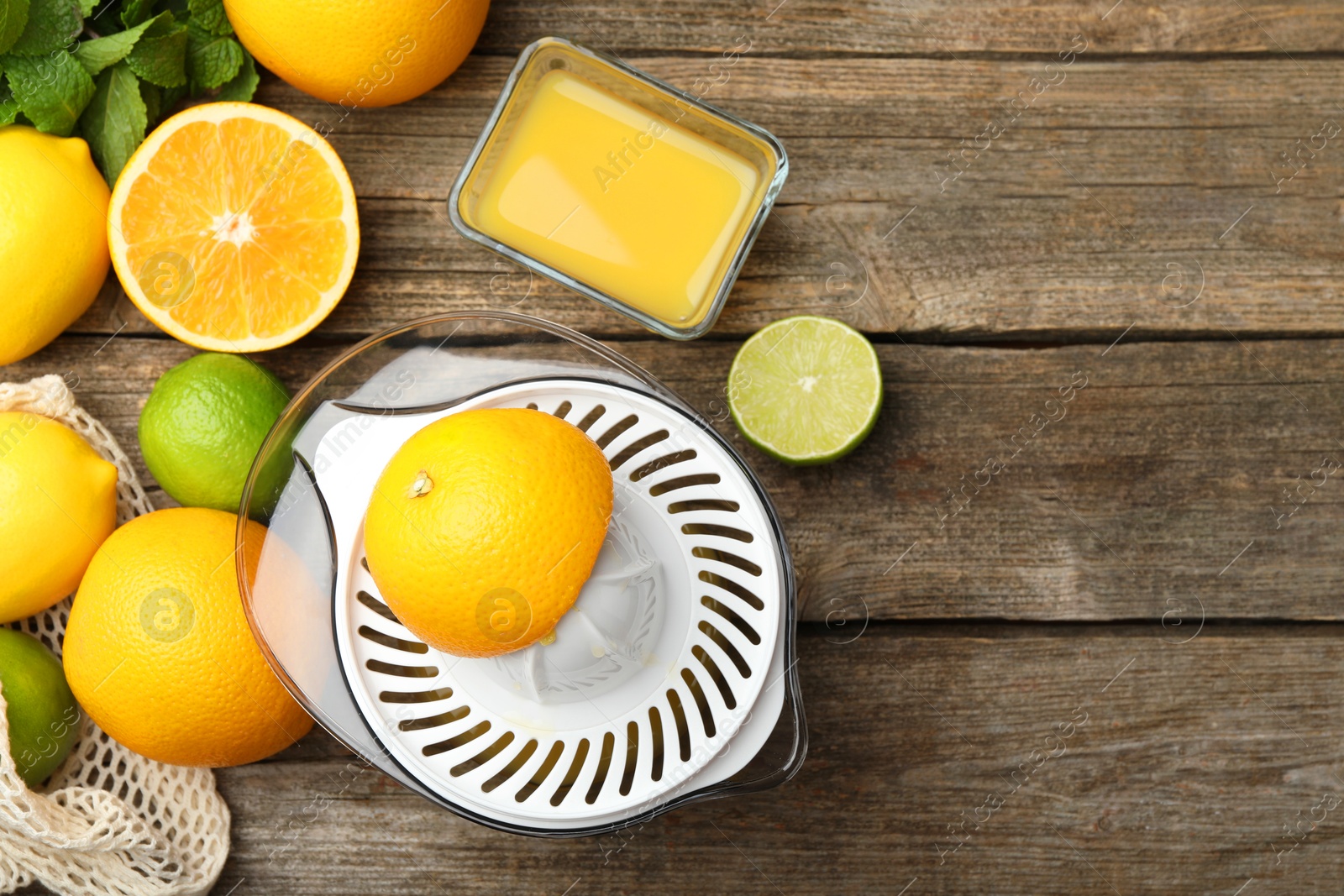 Photo of Plastic juicer, fresh oranges and limes on wooden table, flat lay. Space for text