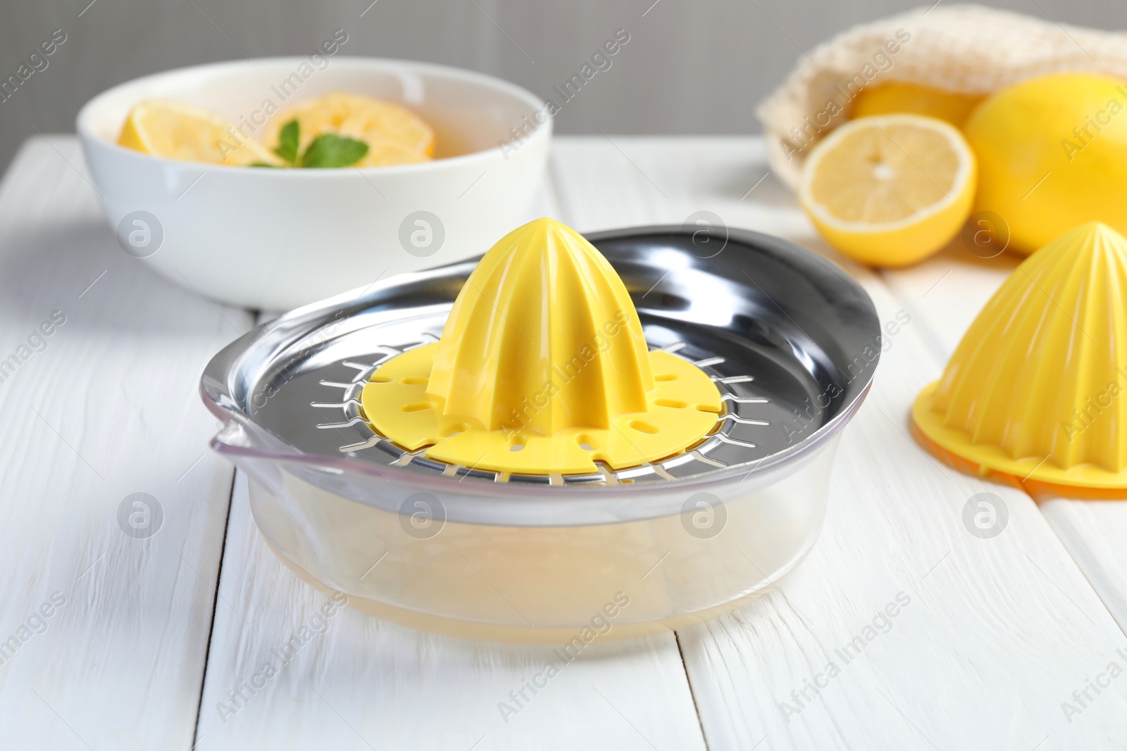 Photo of Plastic juicer and fresh lemons on white wooden table, closeup