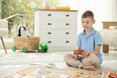 Photo of Creating vision board. Little boy cutting out picture on floor at home