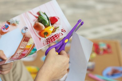 Creating vision board. Little boy cutting out picture indoors, closeup