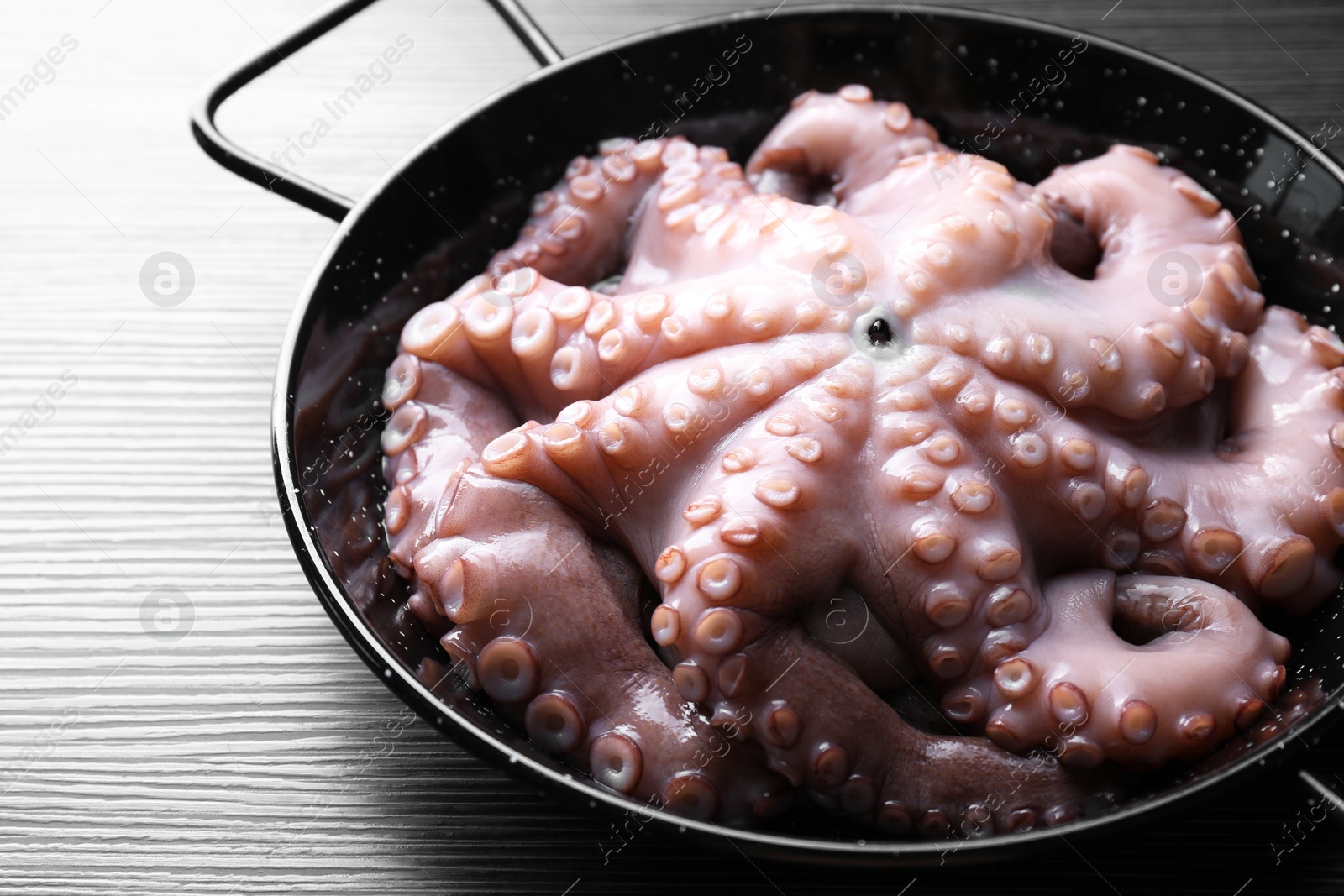 Photo of Fresh raw octopus in frying pan on dark textured table, closeup