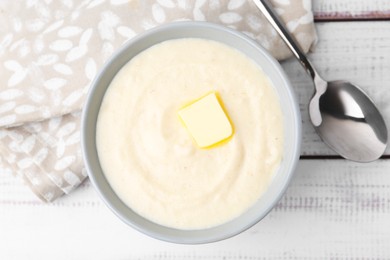 Photo of Tasty cooked semolina porridge with butter and spoon on white wooden table, top view