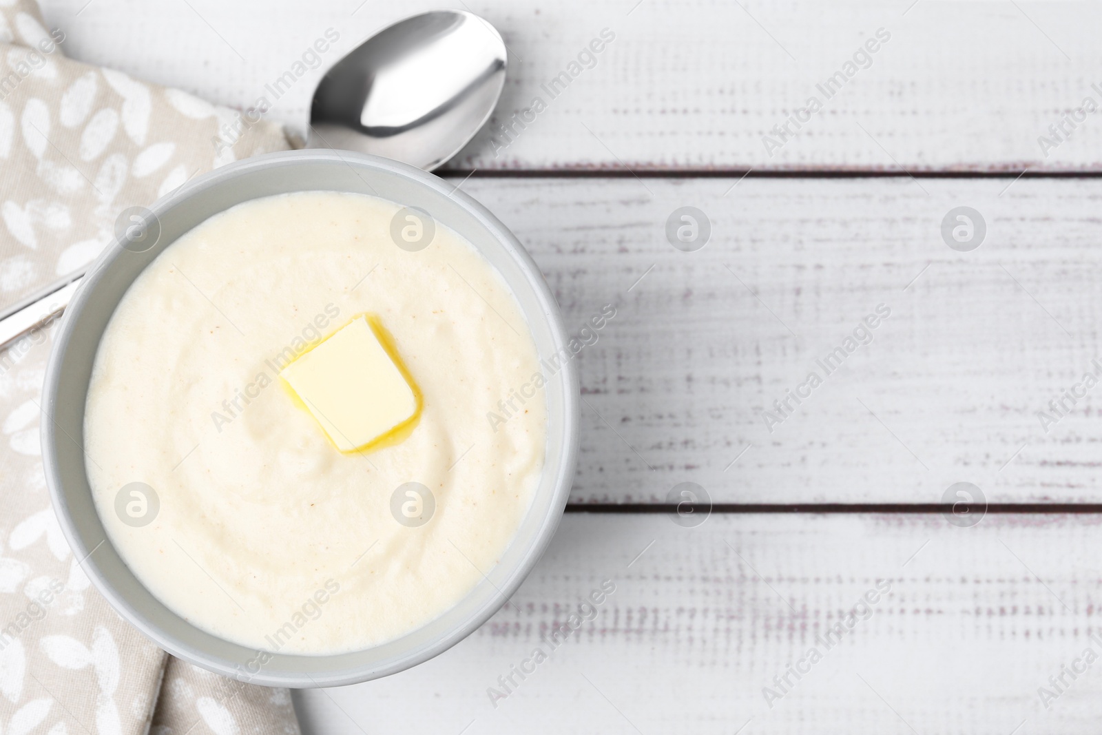 Photo of Tasty cooked semolina porridge with butter and spoon on white wooden table, top view. Space for text