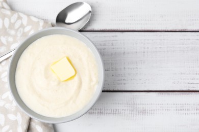 Photo of Tasty cooked semolina porridge with butter and spoon on white wooden table, top view. Space for text