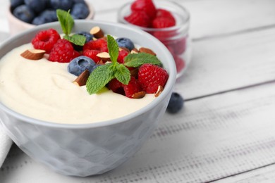 Photo of Tasty cooked semolina porridge with almonds, berries and mint on white wooden table, closeup. Space for text