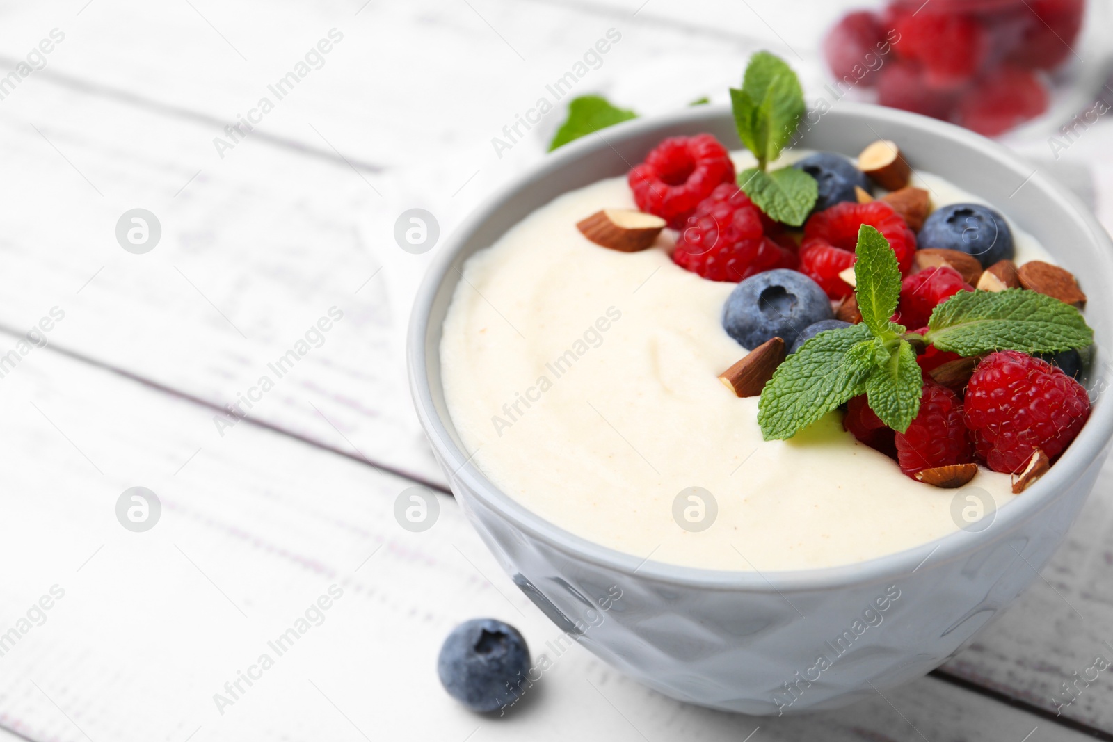 Photo of Tasty cooked semolina porridge with almonds, berries and mint on white wooden table, closeup. Space for text