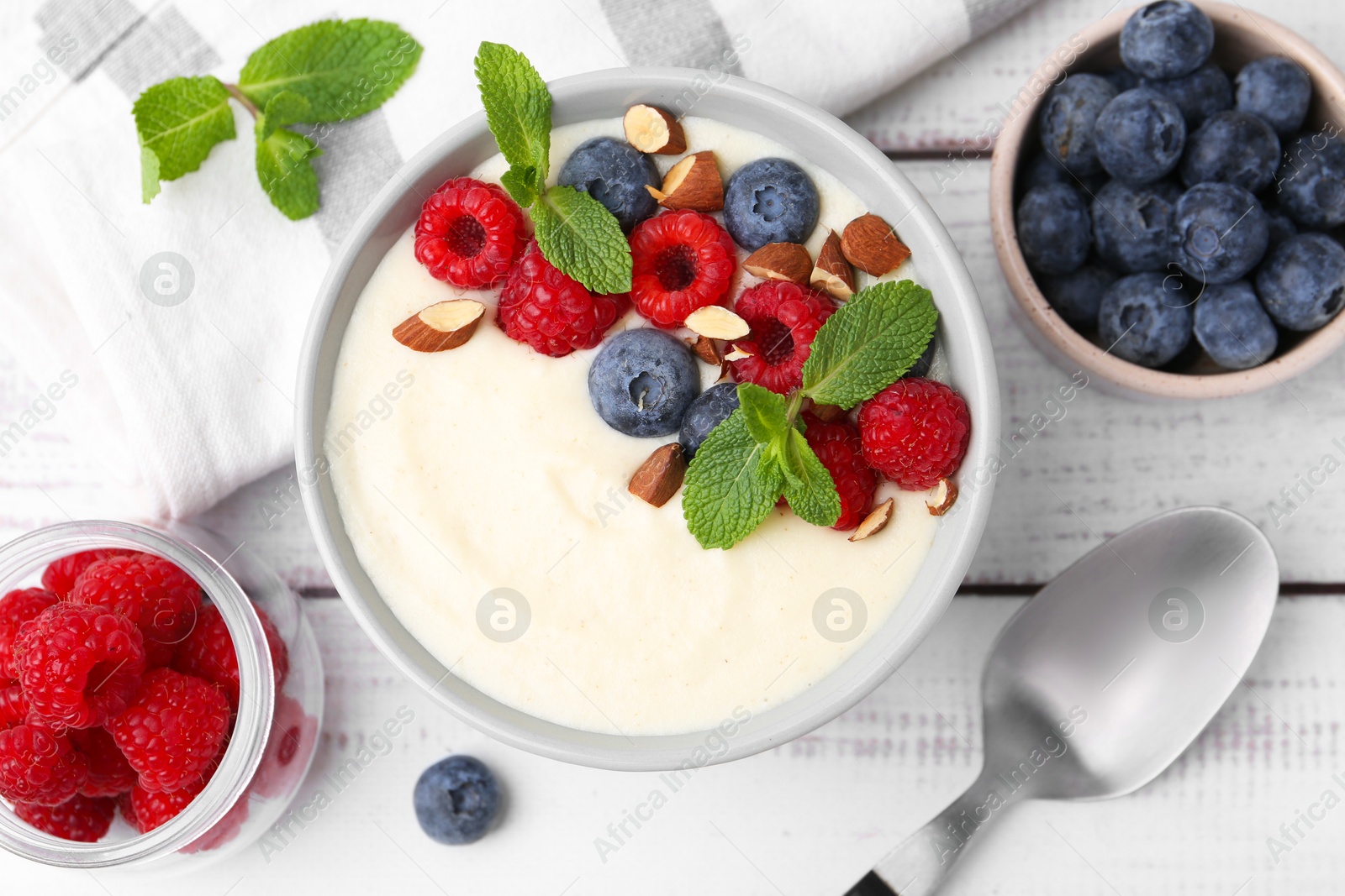 Photo of Tasty cooked semolina porridge with almonds, berries and mint on white wooden table, top view