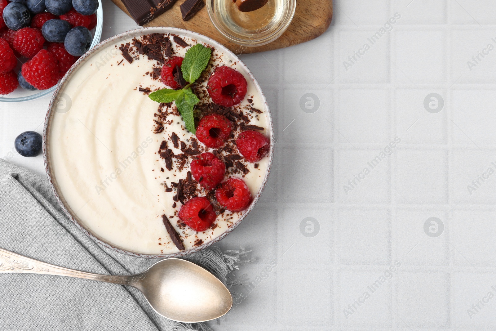 Photo of Tasty cooked semolina porridge with berries served on white tiled table, top view. Space for text