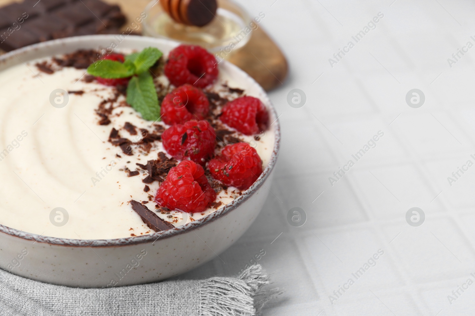 Photo of Tasty cooked semolina porridge with raspberries, chocolate and mint on white tiled table, closeup. Space for text