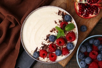 Photo of Tasty cooked semolina porridge with berries, chocolate, mint and pomegranate on wooden table, top view