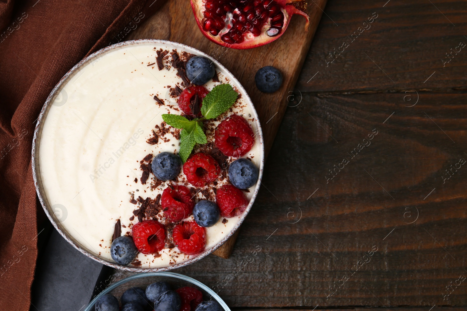 Photo of Tasty cooked semolina porridge with berries, chocolate, mint and pomegranate on wooden table, top view. Space for text