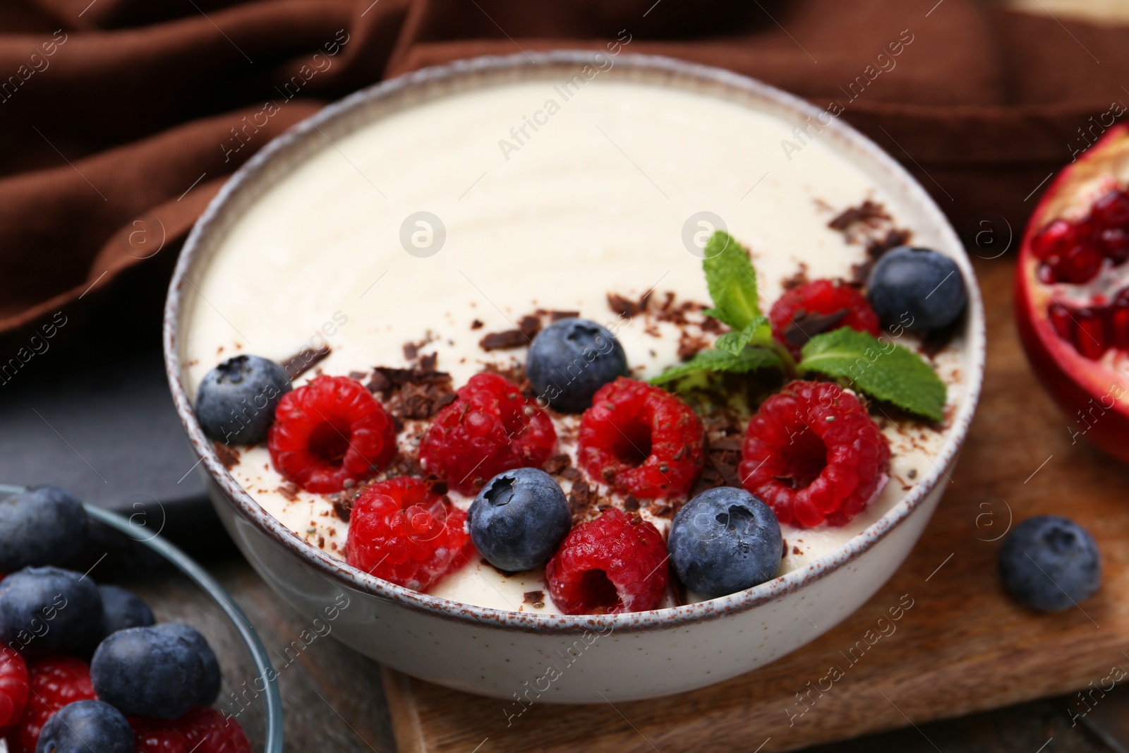 Photo of Tasty cooked semolina porridge with berries, chocolate and mint on table, closeup