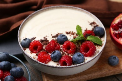 Photo of Tasty cooked semolina porridge with berries, chocolate and mint on table, closeup