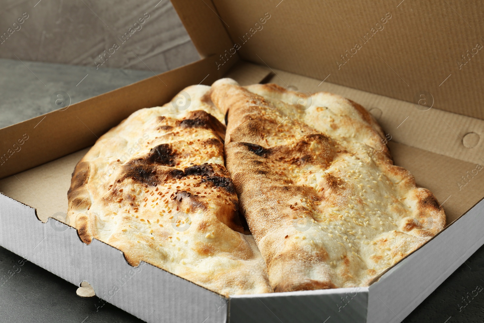 Photo of Delicious calzones in cardboard box on grey table, closeup