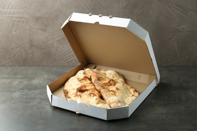 Photo of Delicious calzones in cardboard box on grey textured table