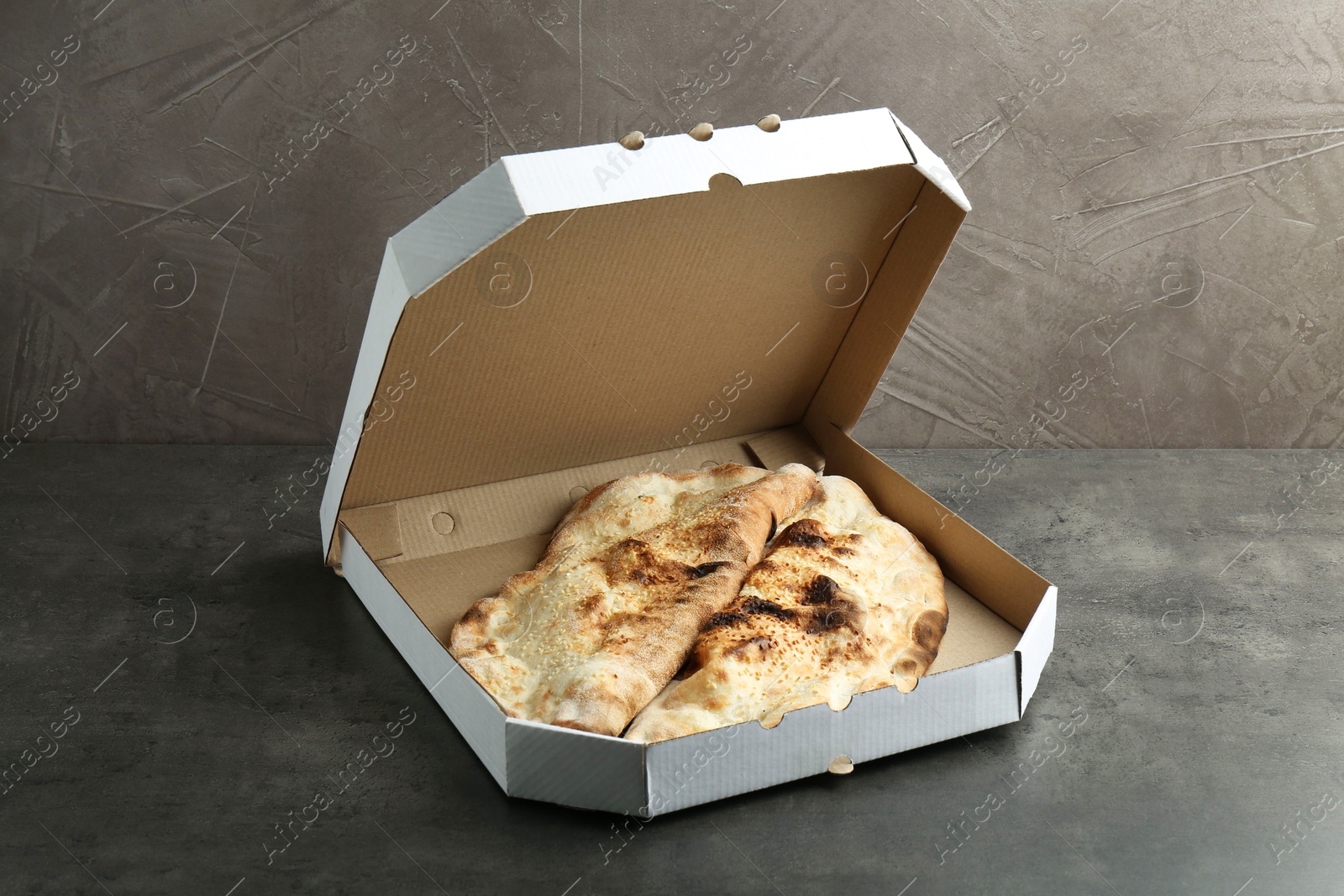 Photo of Delicious calzones in cardboard box on grey textured table