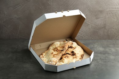 Photo of Delicious calzones in cardboard box on grey textured table