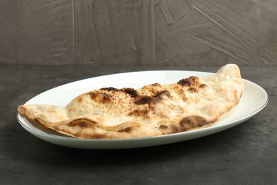 Photo of One delicious calzone on grey textured table, closeup