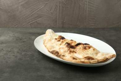 Photo of One delicious calzone on grey textured table, space for text