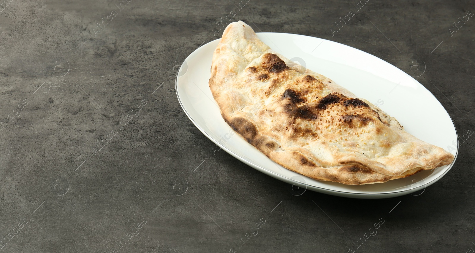 Photo of One delicious calzone on grey textured table, space for text