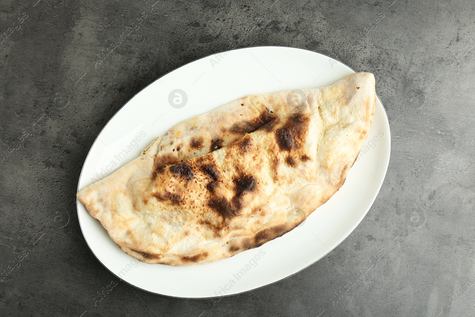 Photo of One delicious calzone on grey textured table, top view