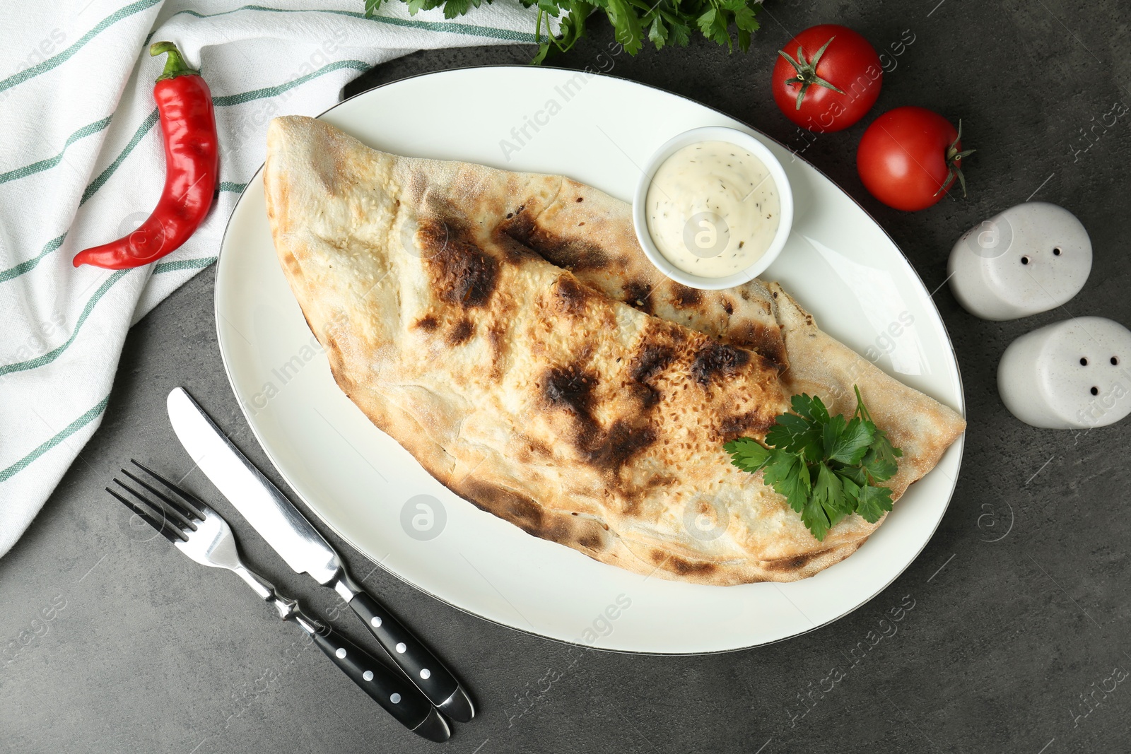 Photo of Delicious calzone served with sauce on grey table, flat lay