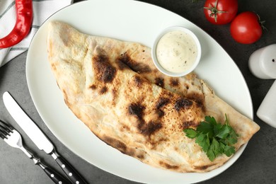 Photo of Delicious calzone served with sauce on grey table, flat lay