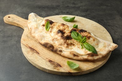 Photo of Delicious calzone with fresh basil on grey textured table