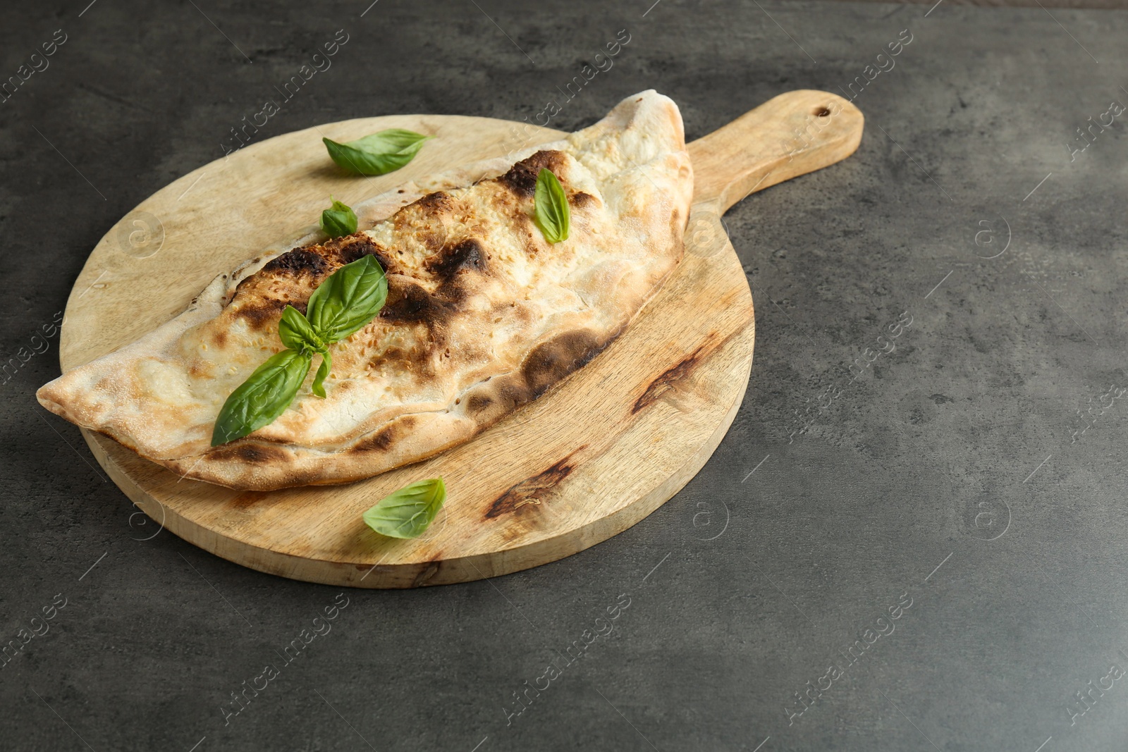 Photo of Delicious calzone with fresh basil on grey textured table, space for text