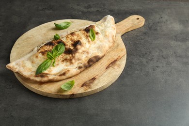 Photo of Delicious calzone with fresh basil on grey textured table, space for text