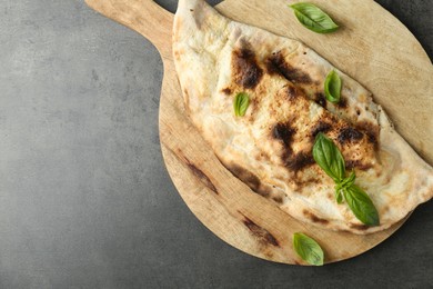 Photo of Delicious calzone with fresh basil on grey textured table, top view. Space for text