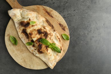 Photo of Delicious calzone with fresh basil on grey textured table, top view. Space for text