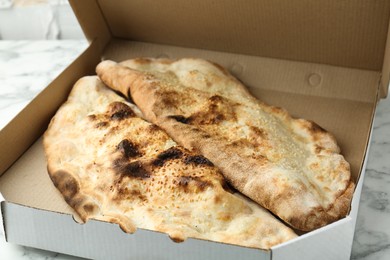 Photo of Delicious calzones in cardboard box on white marble table, closeup