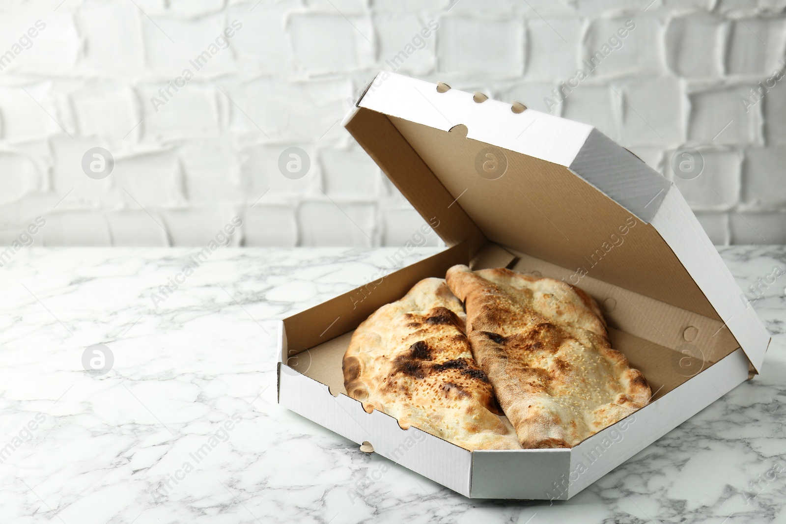 Photo of Delicious calzones in cardboard box on white marble table, space for text