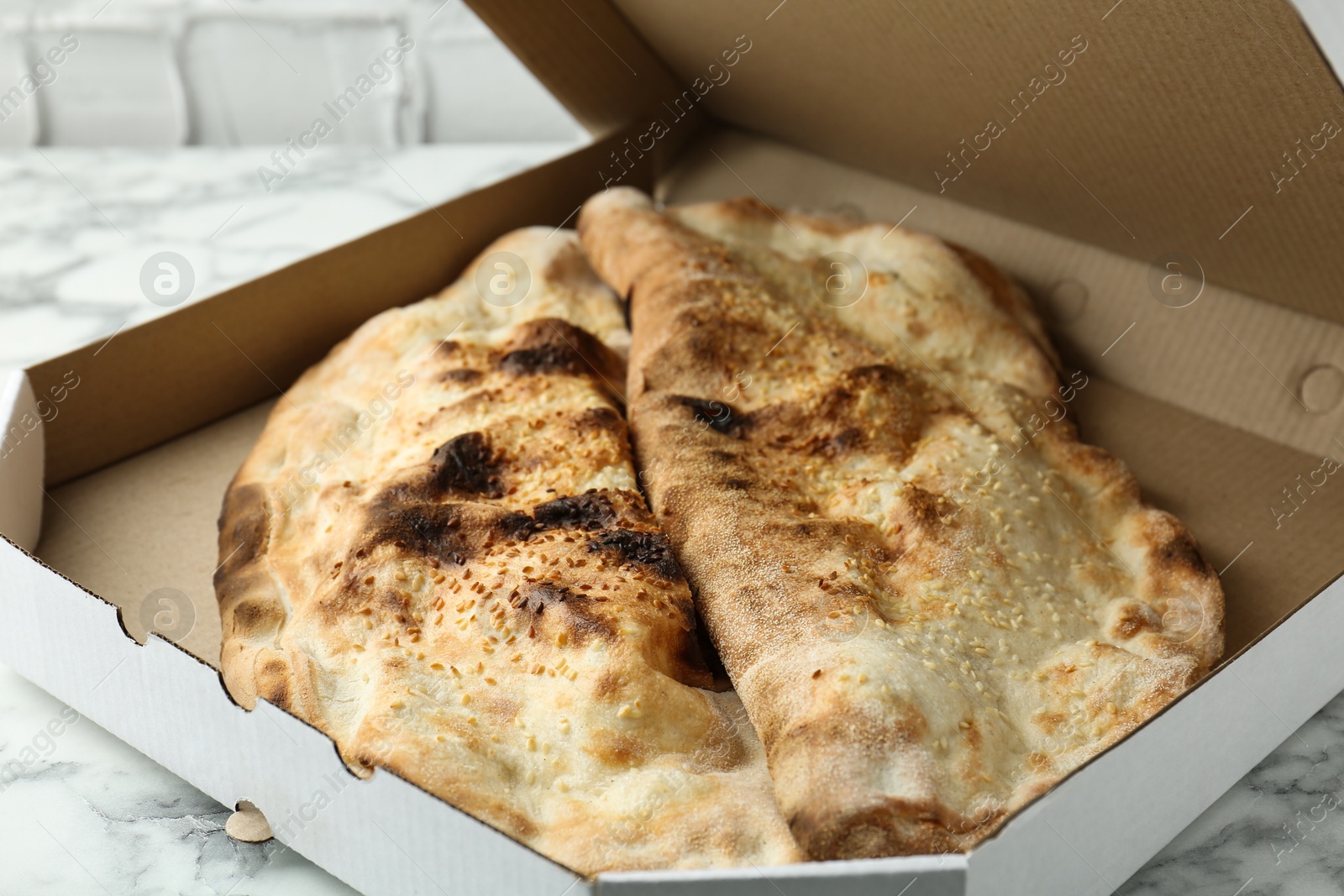 Photo of Delicious calzones in cardboard box on white marble table, closeup