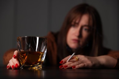 Photo of Alcohol addiction. Woman with glass of whiskey and cigarette at table indoors, selective focus