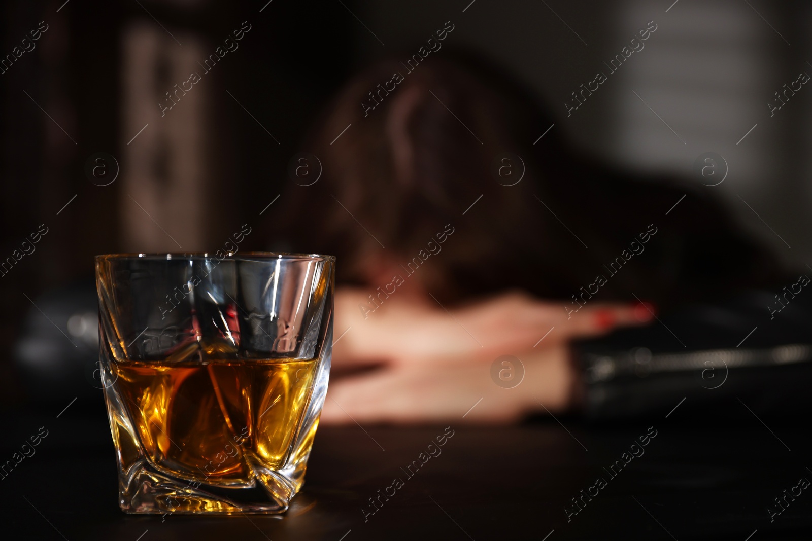 Photo of Alcohol addiction. Woman at table indoors, focus on glass of whiskey