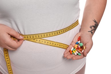 Photo of Plus size woman measuring waist with tape and holding pile of weight loss supplements on white background, closeup