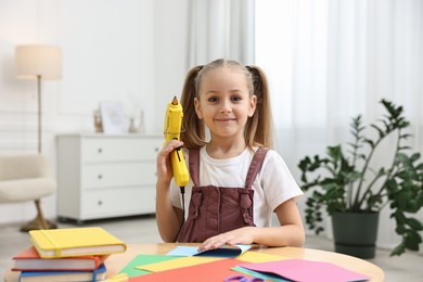 Photo of Portrait of little girl with hot glue gun at table indoors