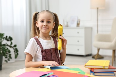 Photo of Portrait of little girl with hot glue gun at table indoors