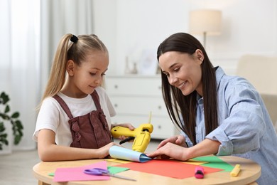 Photo of Mother and daughter with hot glue gun and color paper making craft at table indoors