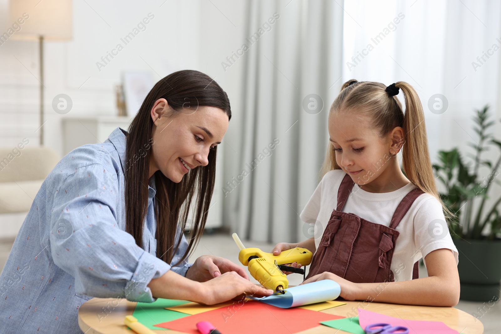 Photo of Mother and daughter with hot glue gun and color paper making craft at table indoors