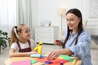 Photo of Mother and daughter with hot glue gun and color paper making craft at table indoors