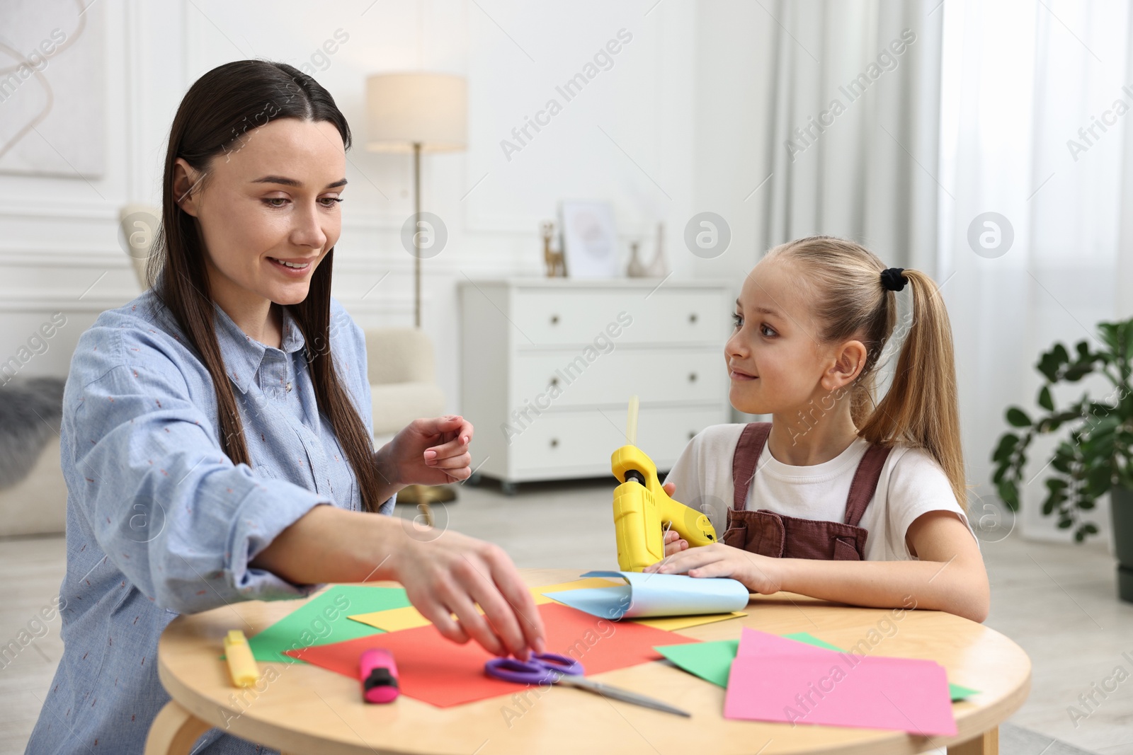 Photo of Mother and daughter with hot glue gun and color paper making craft at table indoors