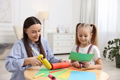 Photo of Mother and daughter with hot glue gun and color paper making craft at table indoors