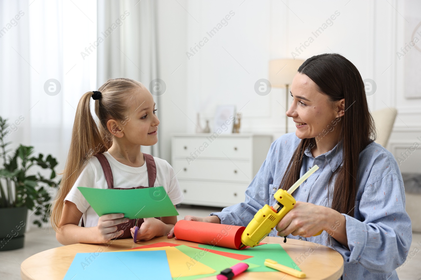 Photo of Mother and daughter with hot glue gun and color paper making craft at table indoors