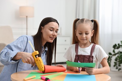 Photo of Mother and daughter with hot glue gun and color paper making craft at table indoors