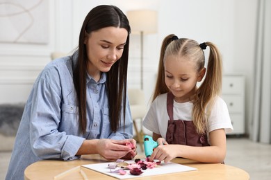 Photo of Mother and daughter with hot glue gun making craft at table indoors