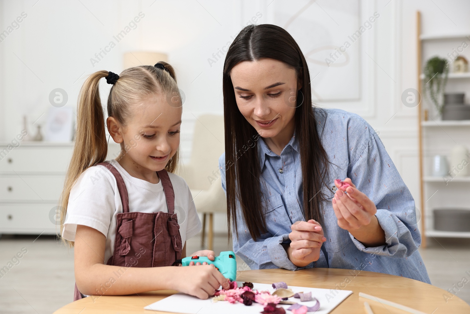 Photo of Mother and daughter with hot glue gun making craft at table indoors